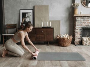 Junge Frau rollt Yogamatte im Wohnzimmer aus