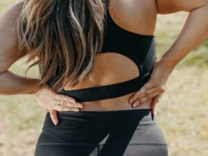 Junge Frau in Sportbekleidung hält sich den schmerzenden Rücken