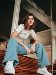 trend-oversized-mode Frau sitzt auf einer Bank und trägt ein weißes Shirt und eine lässige blaue Bootcut-Jeans