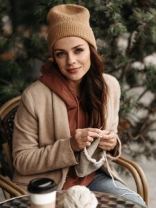 Junge Frau sitzt im Außenbereich eines Cafés und strickt ein Stirnband