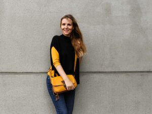 Schichtenlook Damen Pullunder Frau mit gelbem Langarmshirt und schwarzem Pullunder lehnt an der Wand