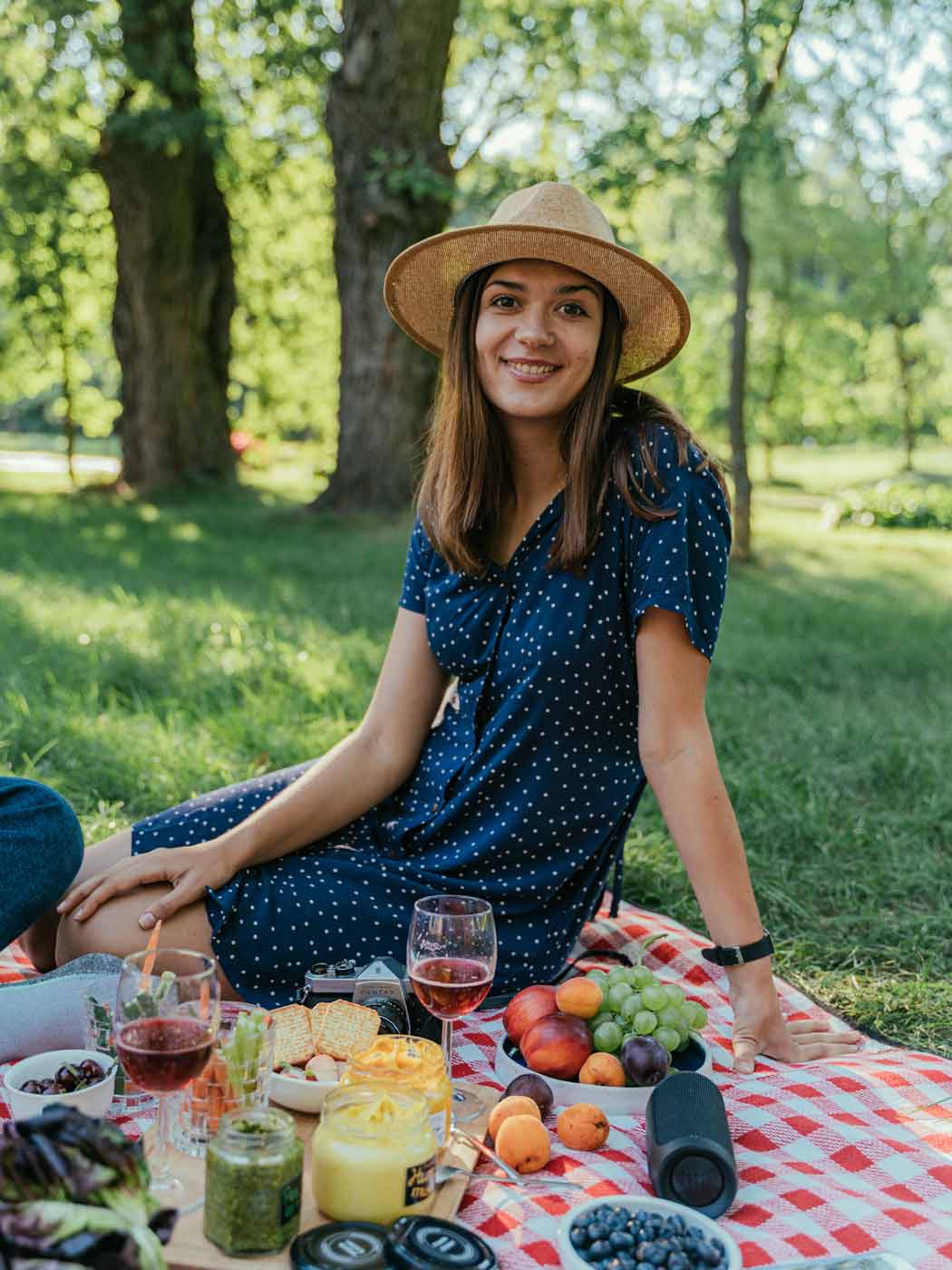 Junge Frau mit Hut sitzt auf einer reich gedeckten Picknickdecke im Grünen