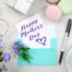 Karte mit Happy Mother's Day liegt auf einem mit Blumen und Süßigkeiten dekorierten Tisch