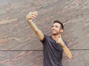 Junger Mann hält das Smartphone zum Selfie von oben vor sich