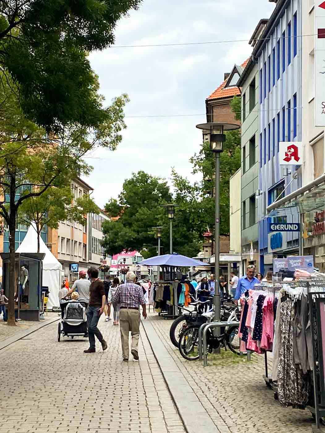 Menschen gehen durch die Hildesheimer Fußgängerzone, an den Seiten Bekleidungsstände