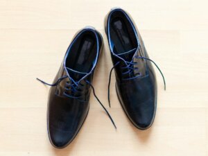 Streckende Herrenschuhe Ein offenes Paar Herren Businessschuhe in Schwarz mit blauen Schnürsenkeln