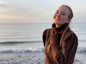 Damen Rollkragen Pullover Junge Frau trägt braunen Rollkragenpullover und posiert vor dem Meer