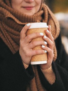 Gesichtslose Frau trägt dicken Schal und hält Coffee-to-go-Becher