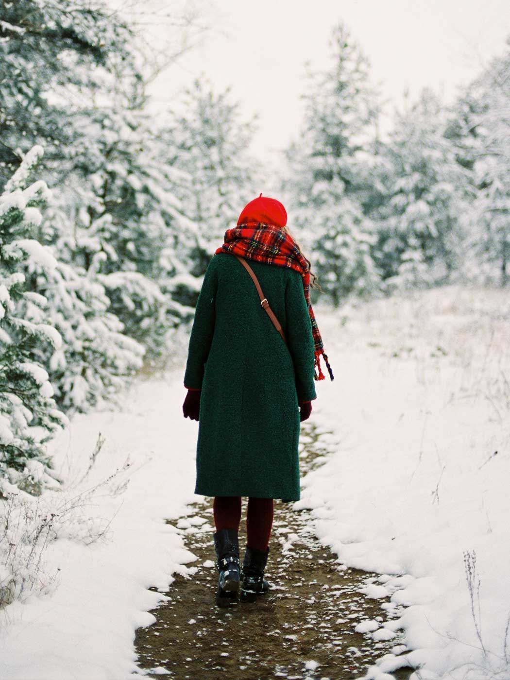 Frau von hinten, die durch einen verschneiten Wald spaziert 