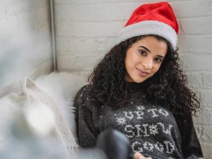 Frau sitzt mit Weihnachtsmütze und winterlichem Pullover an die Wand gelehnt auf dem Sofa