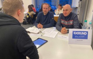 Zwei Männer unterhalten sich an einem Tisch mit einem Studenten