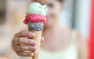 Frau hält eine Eiswaffel mit drei Kugeln in die Kamera