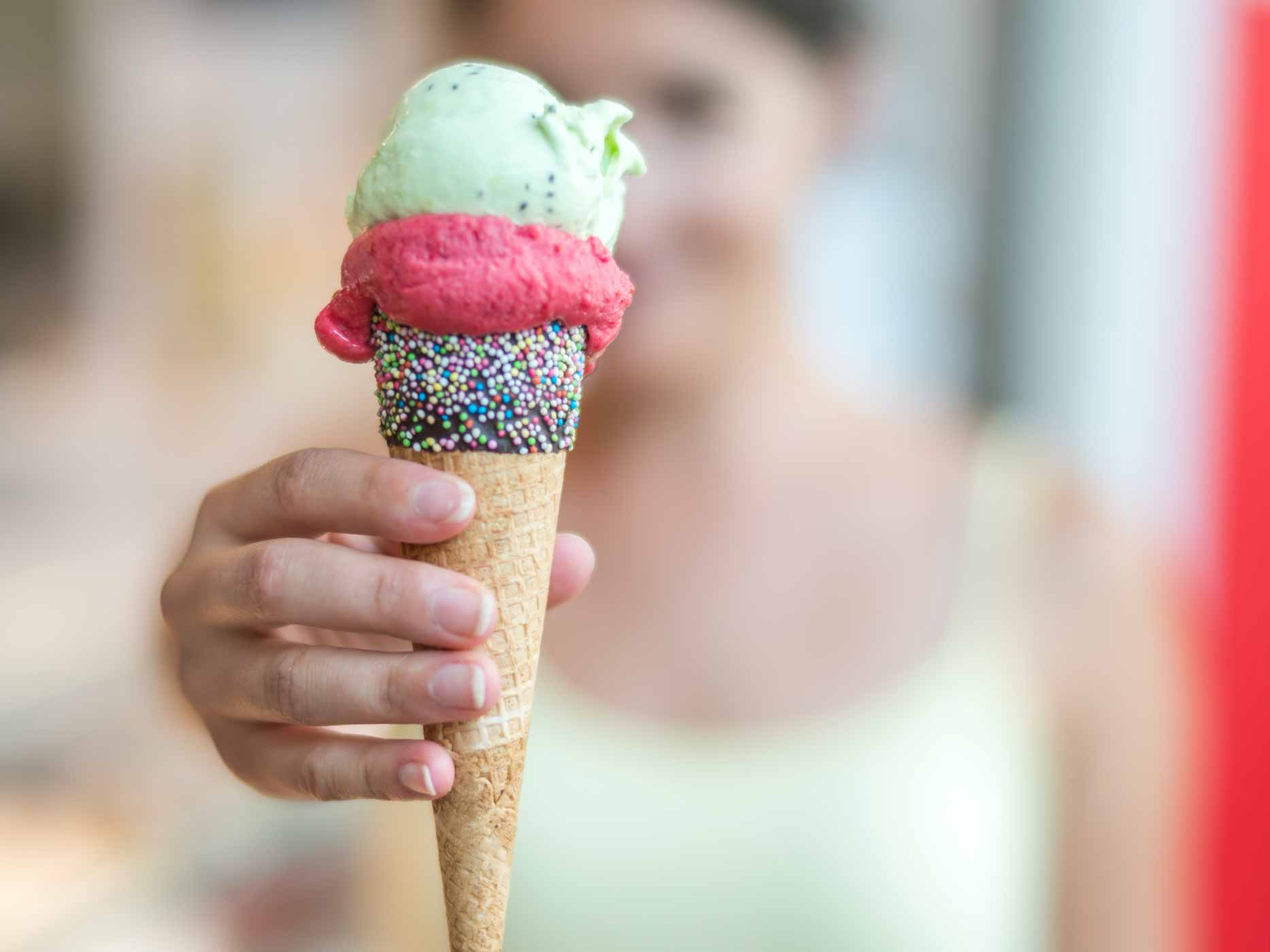 Frau hält eine Eiswaffel mit drei Kugeln in die Kamera