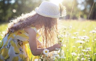Mädchen im Sommerkleid und mit Hut pflückt auf einer sonnigen Wiese Blumen