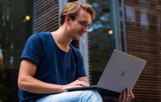 Junger Mann hat draußen einen Laptop auf den Knien