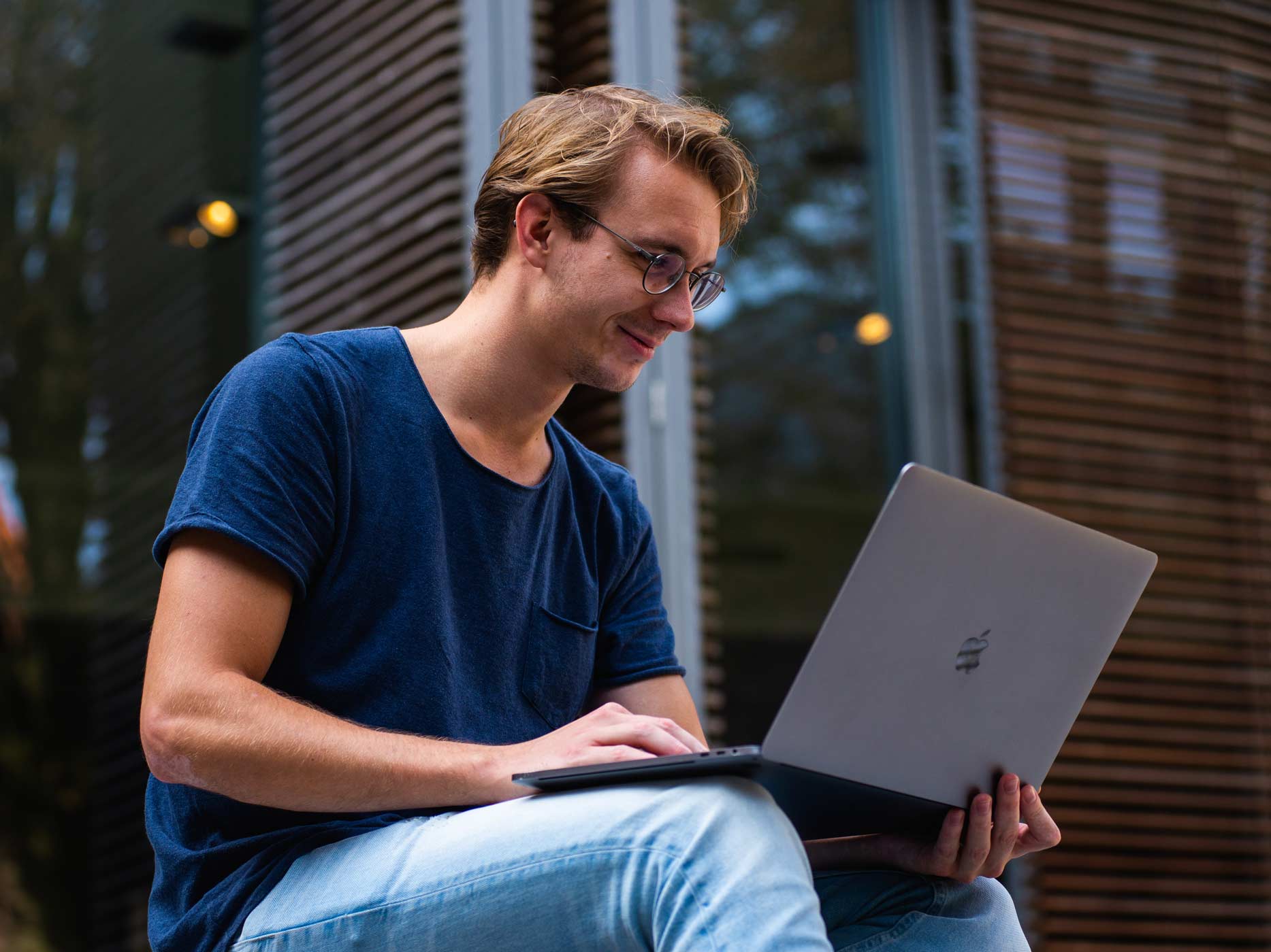 Junger Mann hat draußen einen Laptop auf den Knien