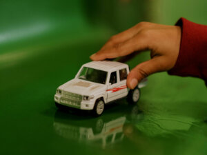 Kinderhand, die vor einem grünen Hintergrund ein weißes Spielzeugauto schiebt.