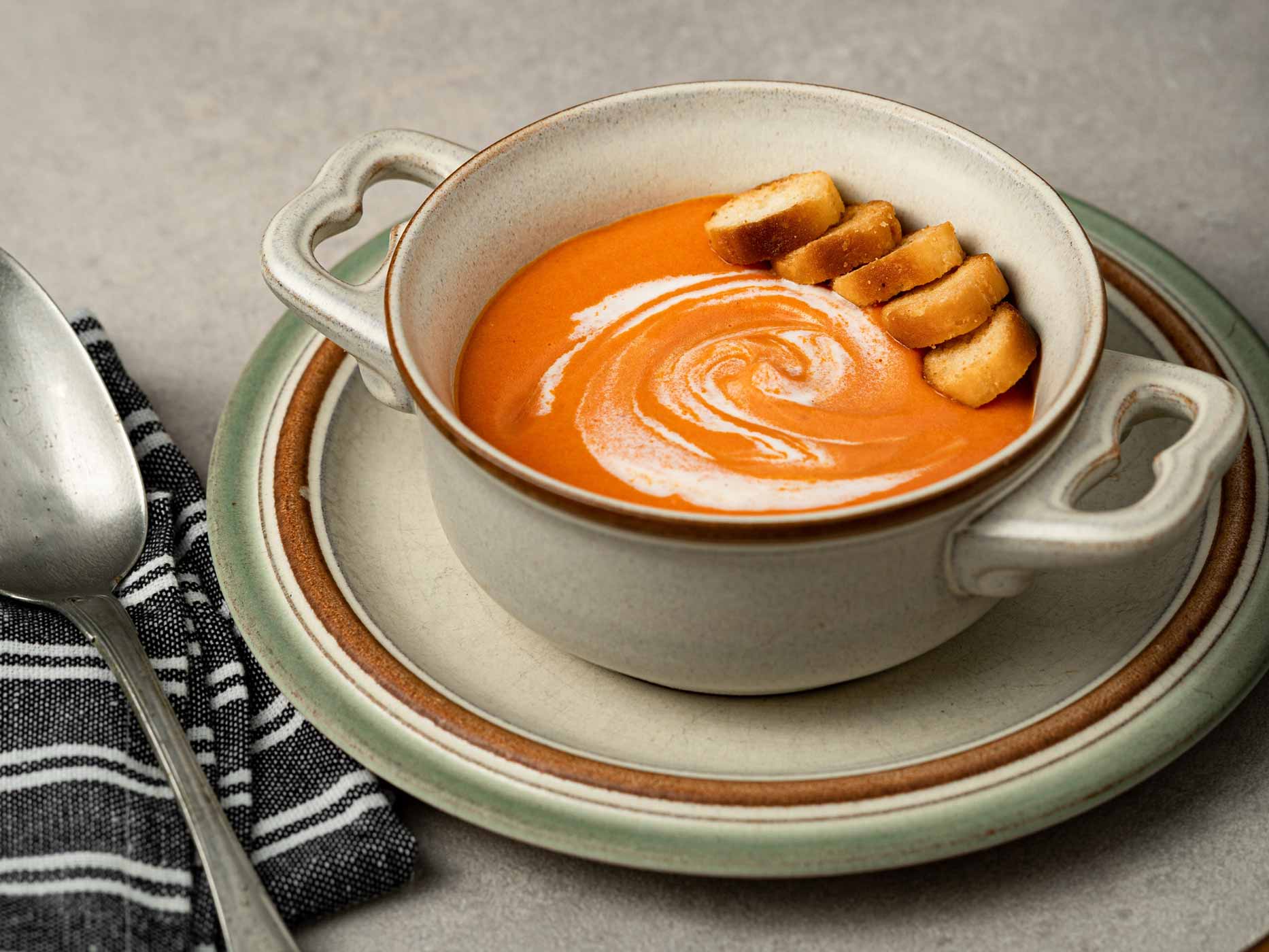 Cremige Kürbissuppe mit Croutons und Sahne verfeinert in einer Suppentasse.