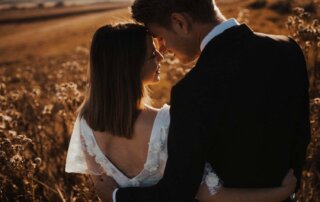 Ein Brautpaar steht im Sonnenuntergang vor einem Getreidefeld und lehnt verliebt die Köpfe aneinander