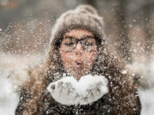 Frau mit Mütze und Handschuhen pustet Schnee weg