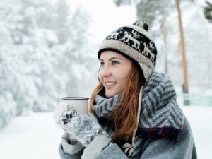 Frau mit Norwegermütze in Schneelandschaft trinkt Heißgetränk