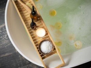 Eine mit Wasser gefüllte Badewanne, auf der ein Brett mit Bürsten, Salzen, Ölen und Kerzen montiert ist