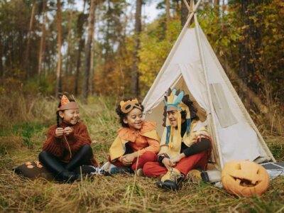 Kinder sitzen als Indianer und Tiere verkleidet vor einem Zelt im Wald