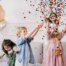 Kinder haben Partyhüte auf und schmeißen buntes Konfetti in die Luft
