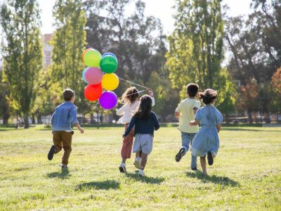 Kinder laufen mit Ballons in der Hand durch einen Park