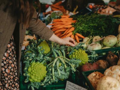 Frau steht vor einem Marktstand mit viel buntem Gemüse