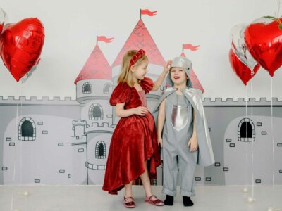 Zwei Kinder haben sich als Prinzessin und Ritter verkleidet und stehen vor einer aufgemalten Ritterburg