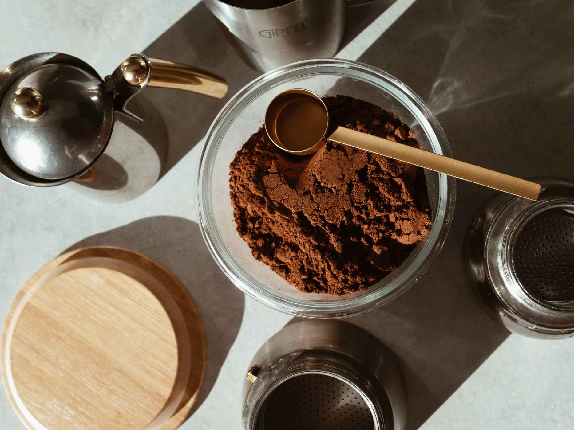 Kaffeepulver mit Lot in einem Glas, darum stehen weitere Kaffeeutensilien