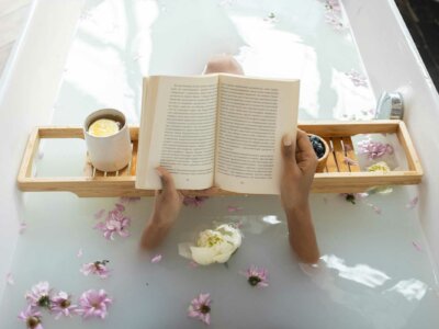 Frau liegt in einer Badewanne mit Blumen und Kerzen und liest ein Buch