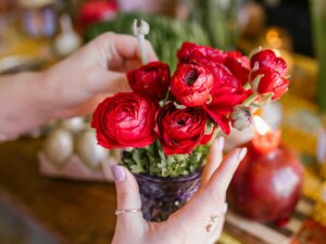 Frauenhände richten Blumen in einer Vase an, im Hintergrund liegt Frühlings- und Osterdeko