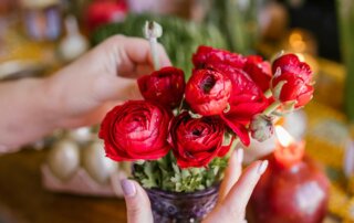 Frauenhände richten Blumen in einer Vase an, im Hintergrund liegt Frühlings- und Osterdeko