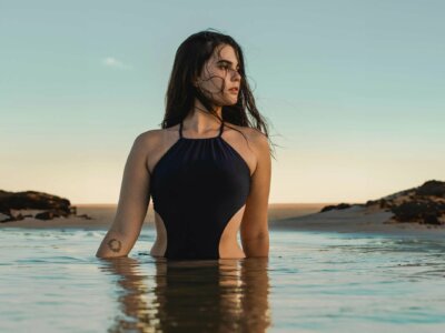 Frau steht im Meer und trägt schwarzen Badeanzug mit seitlichen Cut-Outs