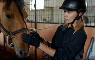 Mädchen im Stall mit Reitkappe und Handschuhen, das ein Pferd streichelt