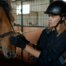 Mädchen im Stall mit Reitkappe und Handschuhen, das ein Pferd streichelt