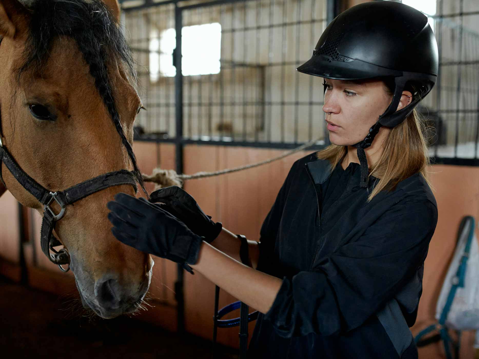 Mädchen im Stall mit Reitkappe und Handschuhen, das ein Pferd streichelt