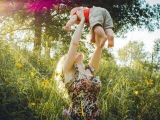 Frau steht im Gras und wirft ihr Baby hoch