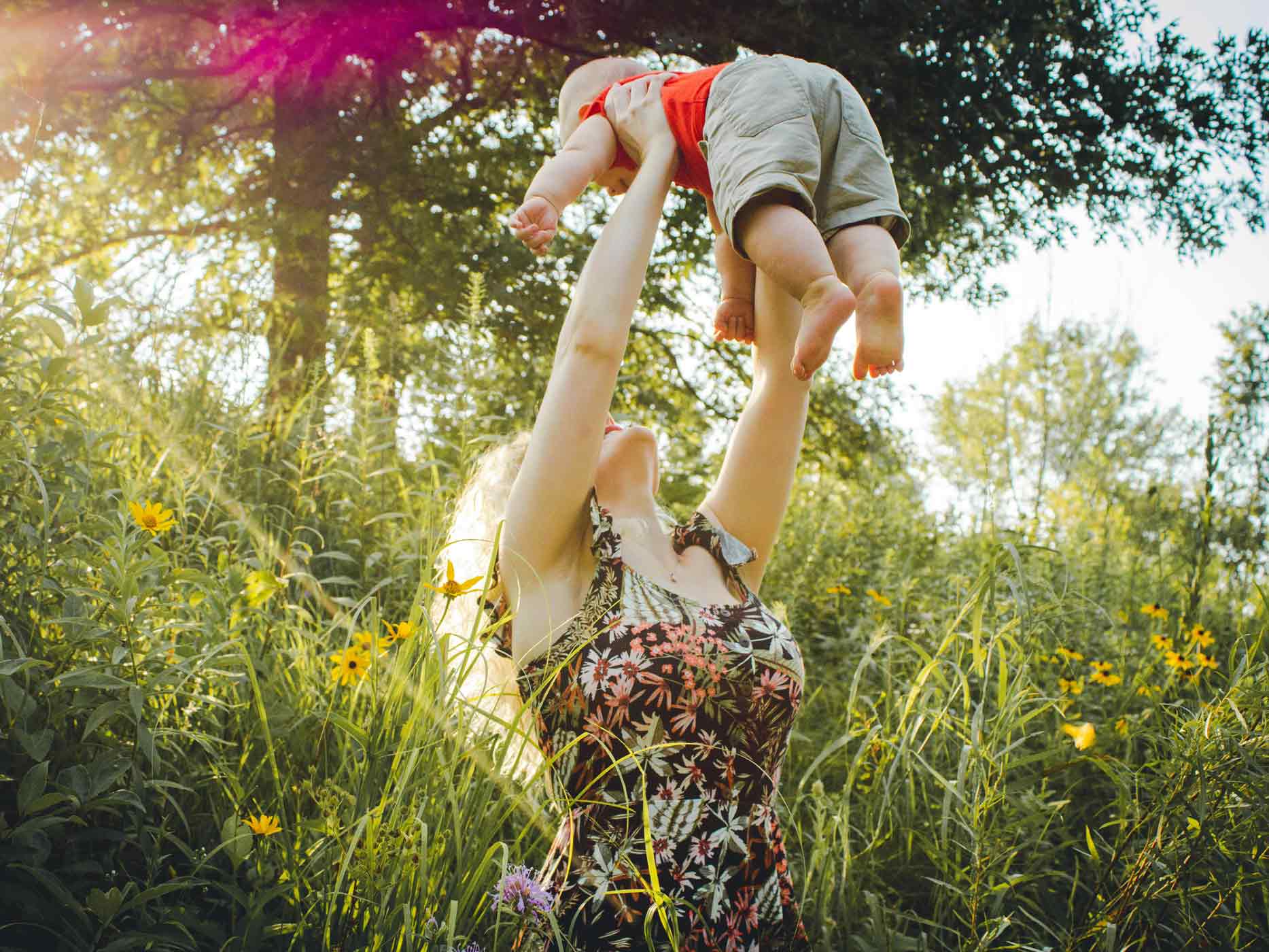 Frau steht im Gras und wirft ihr Baby hoch