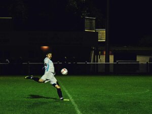 Spieler kickt Fußball im dunklen Stadion.