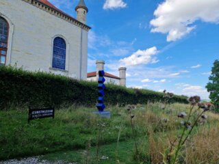Schloss Derneburg mit Skulptur und Eingangsschild vor blauem Himmel