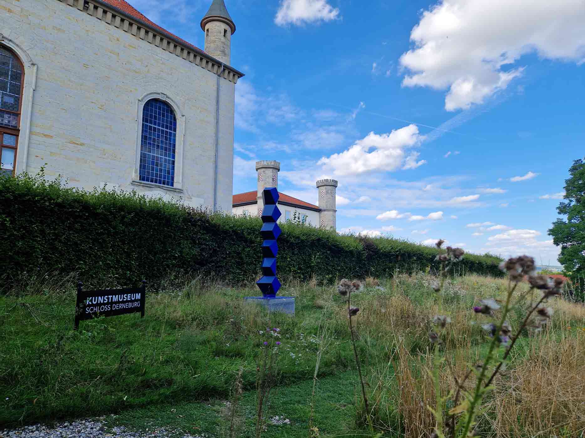 Schloss Derneburg mit Skulptur und Eingangsschild vor blauem Himmel