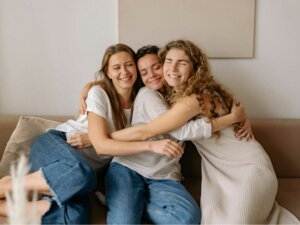 Drei Frauen sitzen auf einem Sofa, umarmen sich und lächeln für die Kamera.