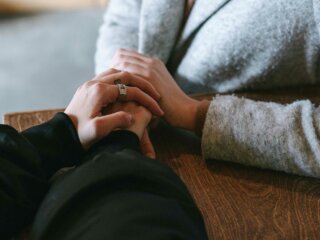 Eine Frau hält die Hände von einer anderen Frau auf tröstende Weise.