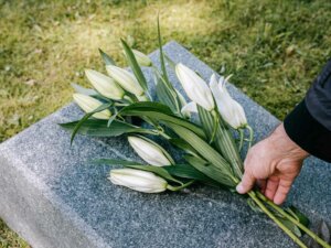 Eine Hand legt weiße Lilien auf eine Grabplatte.
