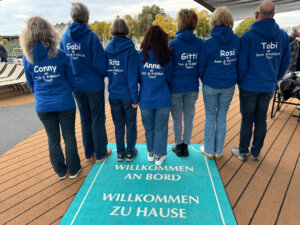 Sieben Personen in den gleichen dunkelblauen Sweatshirts stehen mit dem Rücken zur Kamera.