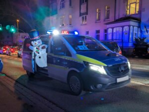 Ein Polizeiauto aus dessen hinterer Schiebetür ein aufblasbarer Schneemann guckt fährt vorbei.