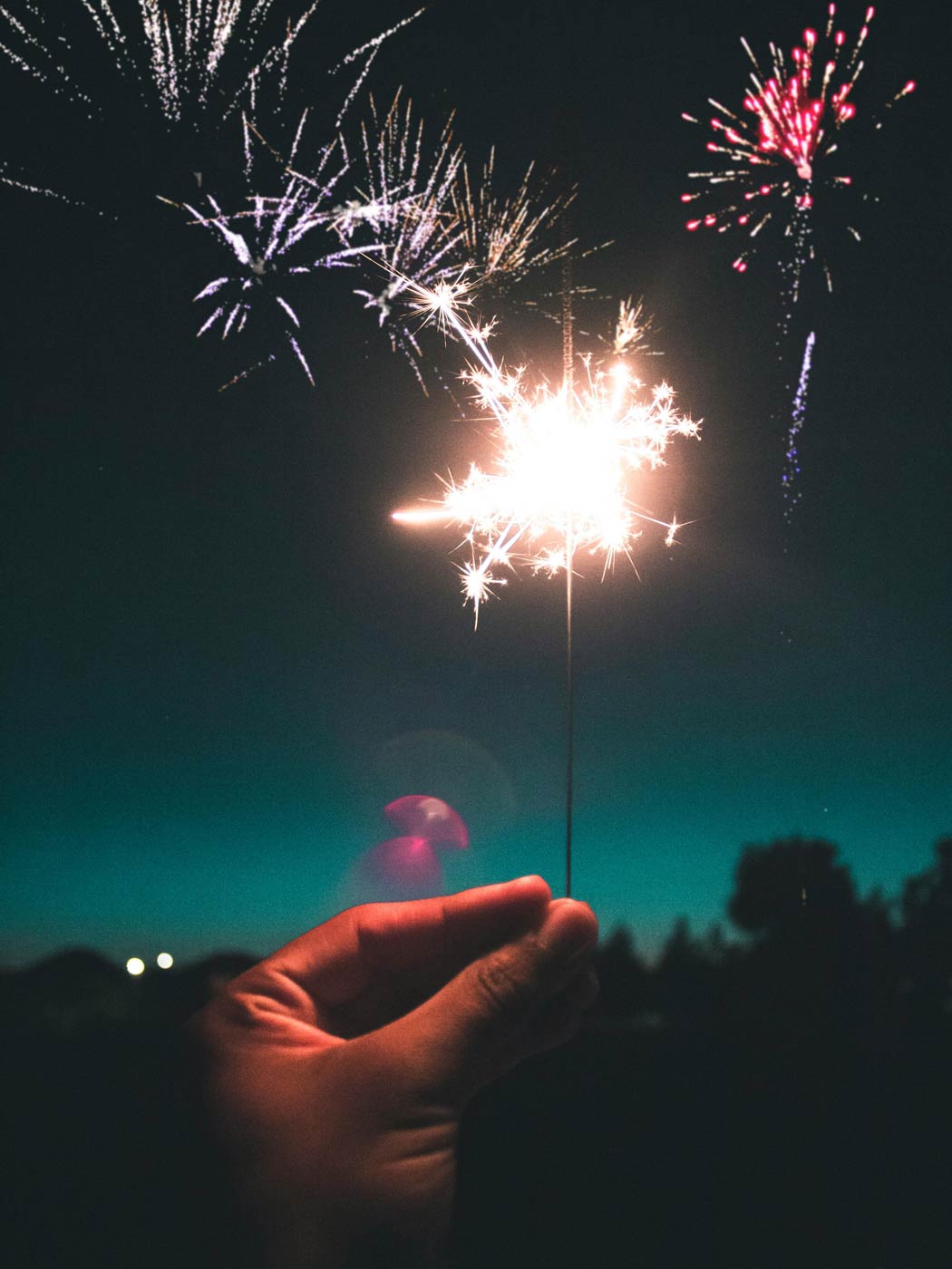 Eine Wunderkerze und leuchtendes Feuerwerk vor dunklem Nachthimmel
